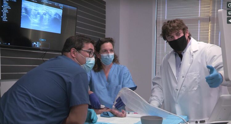 Three doctors are looking at the screen showing x-rays