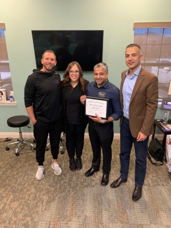 Dr. Bilal Islam standing next three team members holding a certificate of completion for performing over 100 carpal tunnel release with ultrasound guidance procedures. 